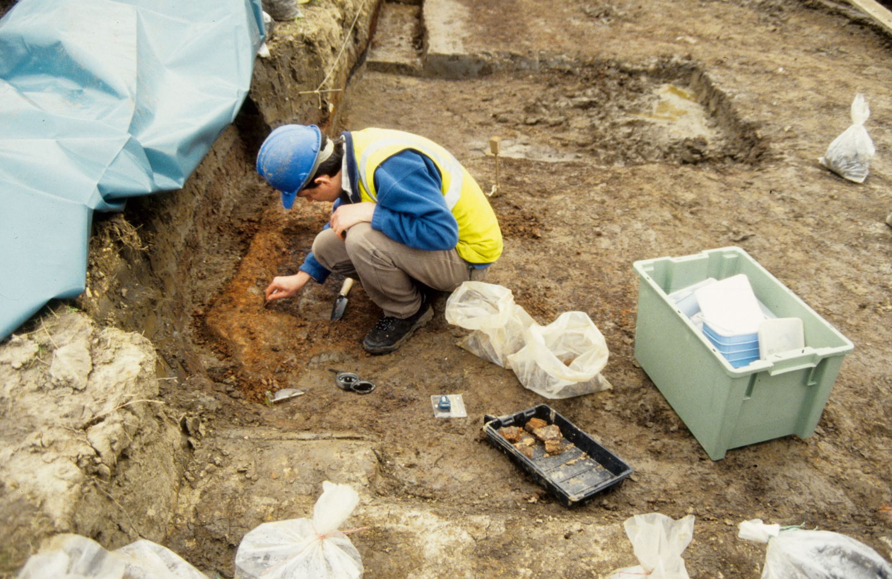 A photograph of a large archaeological dig site where a person, surrounded by equipment, works on some exposed deposits.