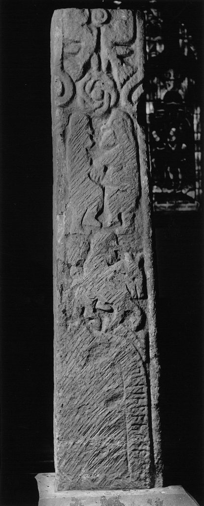A photo of a stone pillar, on which carvings can be seen, including the image of a person riding a horse.