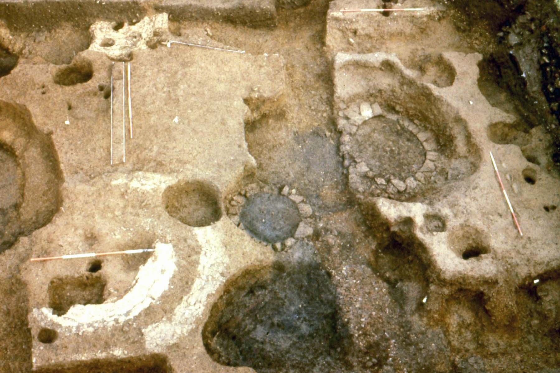 A photograph of an archaeological excavation, showing two circular structures with stone foundations.