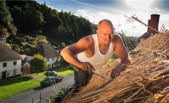 Photograph of a thatcher, Andrew Osmond, working on a thatched roof in Dorset