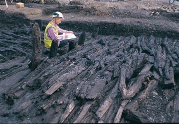 Archaeologist recording a collection of wooden timbers.