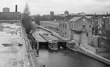 Black and white photograph of a canal lock with buildings on either side