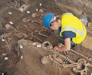 Archaeologists wearing a hard hat, excavating skeletons.